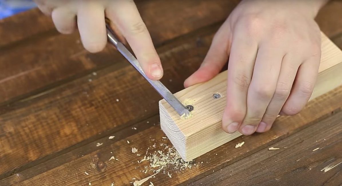 À l'aide d'un ciseau ou d'un ciseau, une surface en bois est traitée, située dans la zone de la tête de vis