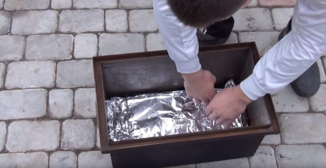 Après cela, la plaque à pâtisserie est installée dans le fumoir au-dessus des copeaux de bois.