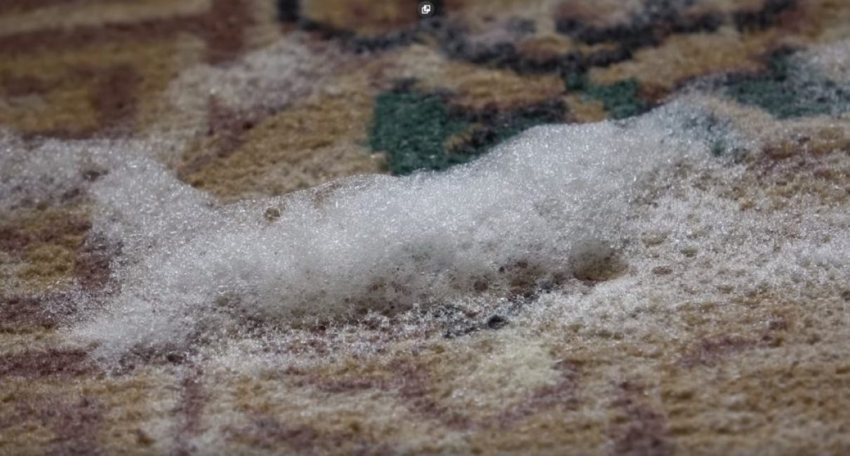 Soda en mousse et détergent à vaisselle sur la surface de la moquette