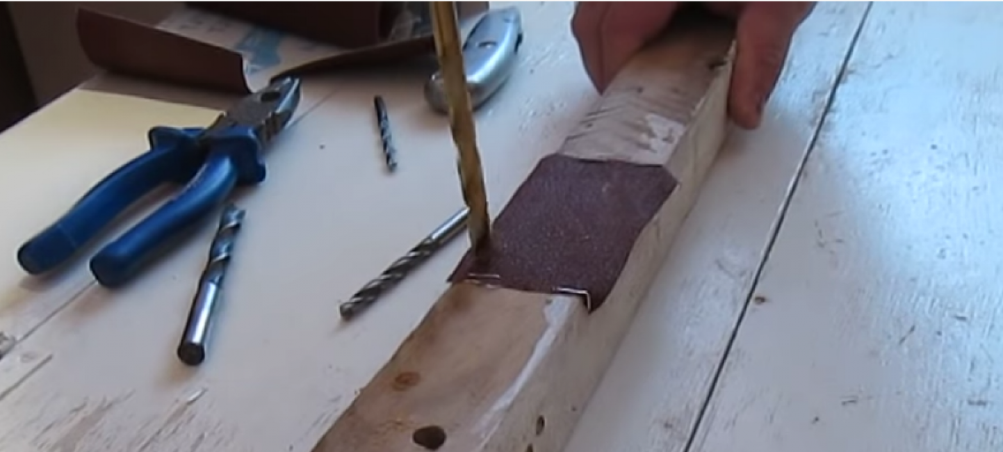 Nous prenons un tournevis, posons une perceuse émoussée dessus et en mode inverse, nous commençons à percer des trous dans la barre à travers le papier de verre fixe.